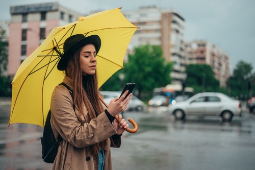woman checking weather app on phone under umbrella