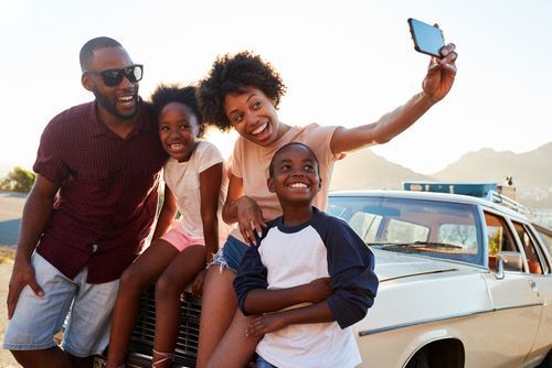 Family taking selfie next to their car on a road trip