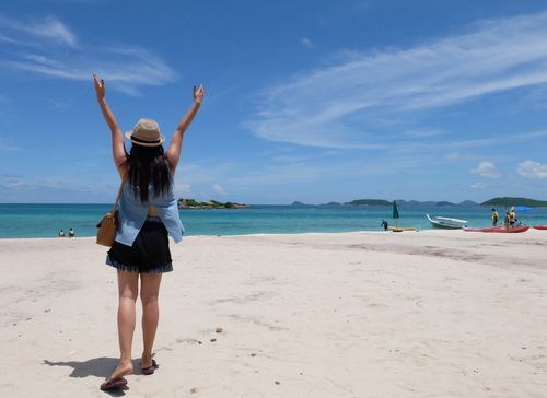 A woman walking on the beach with her hands held up in the air.