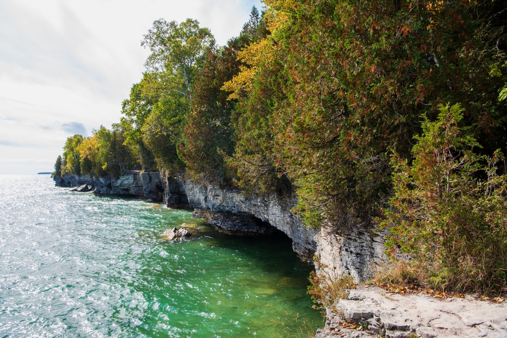 Rocky coastline covered in thick trees along Lake Michigan with its glistening blue-green water.