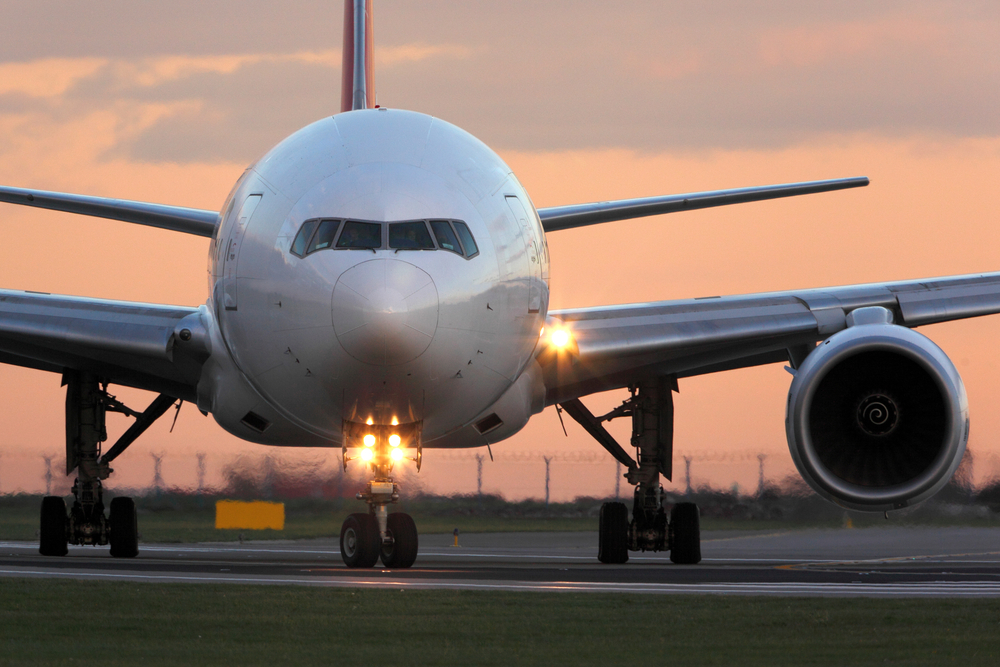 Modern passenger airplane taking off at airport during sunset.