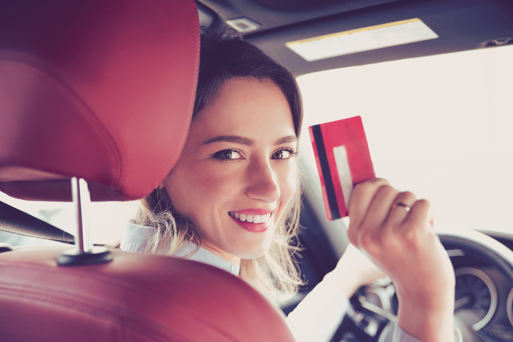 Happy woman sitting inside her new car showing credit card