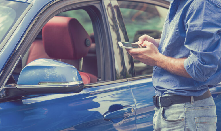 Man using smart phone standing next to a car.