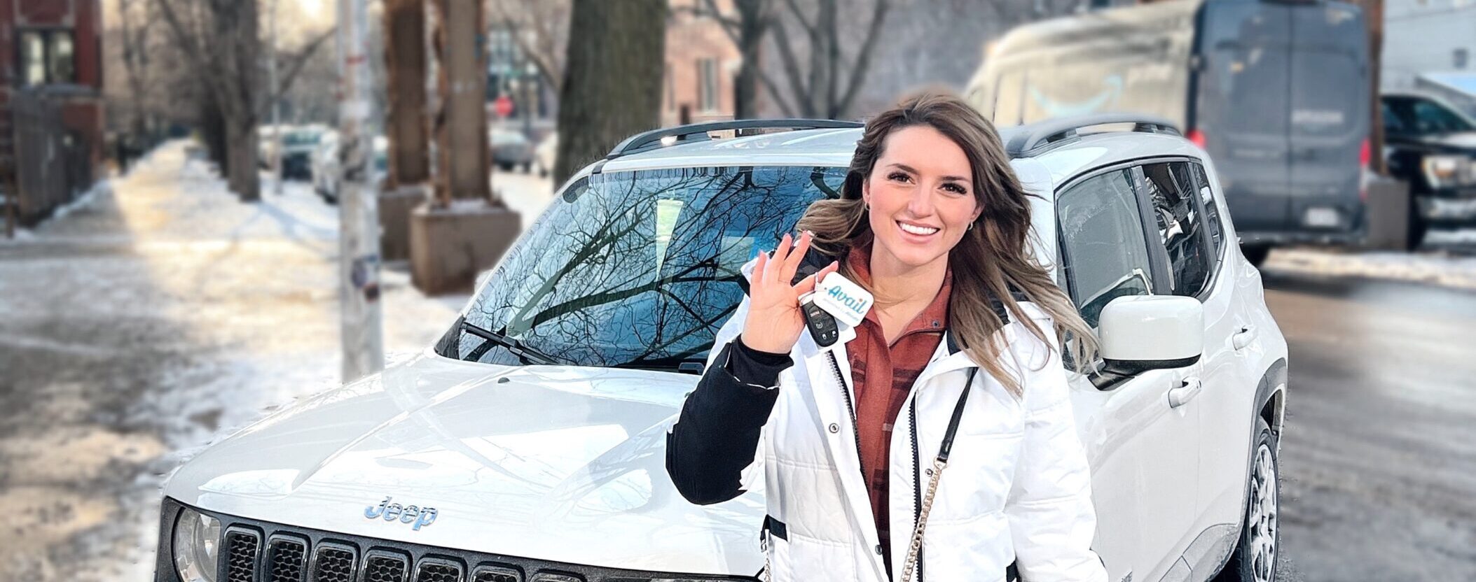 Smiling woman stands in front of a white car and holds a key chain with the Avail car sharing logo.