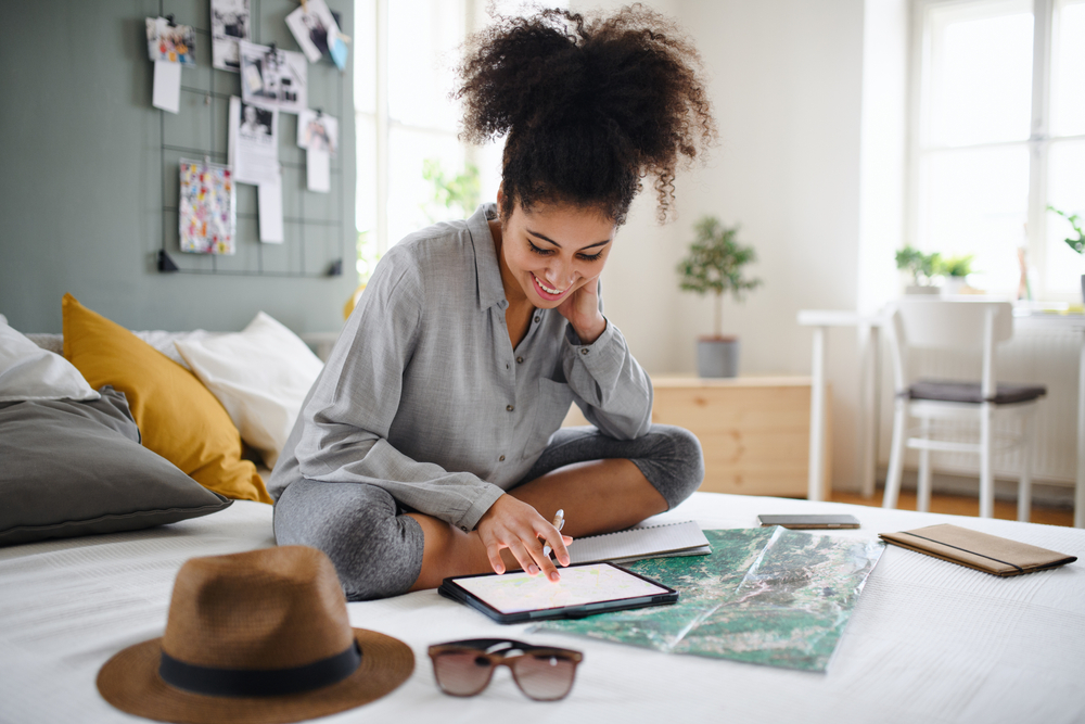 Young woman with tablet and map indoors at home, planning a trip.
