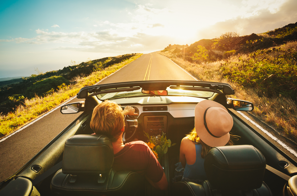 View from behind of a couple driving down an open road in a convertible.