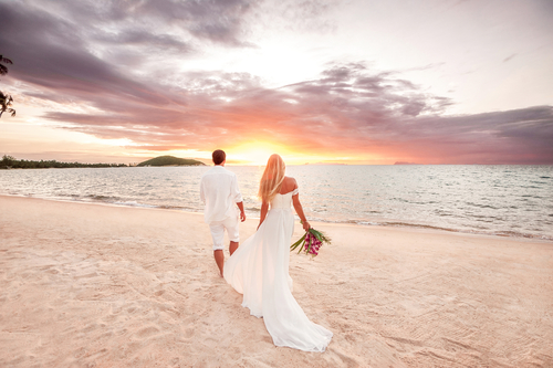 Bride and groom walking on a beach at sunset.