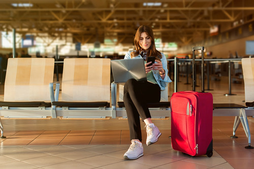 Woman sitting at airport with laptop, phone, and luggage