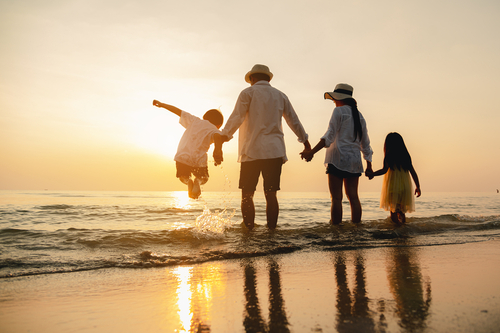 Family of four holding hands and walking in the ocean water at sunset.