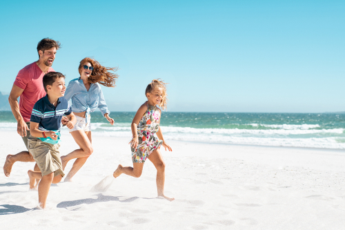 Family of four running along a white sandy beach.