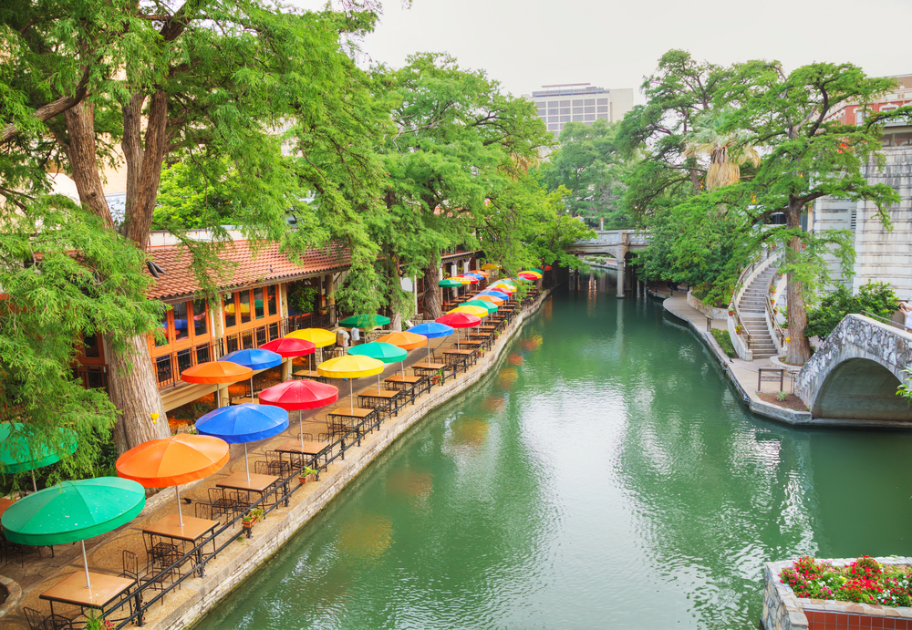 A river lined by colorful umbrellas over tables and chairs.