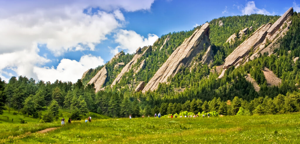 Flatirons in Boulder, Colorado. Several rock formations jutting out of the ground, surrounded by greenery.