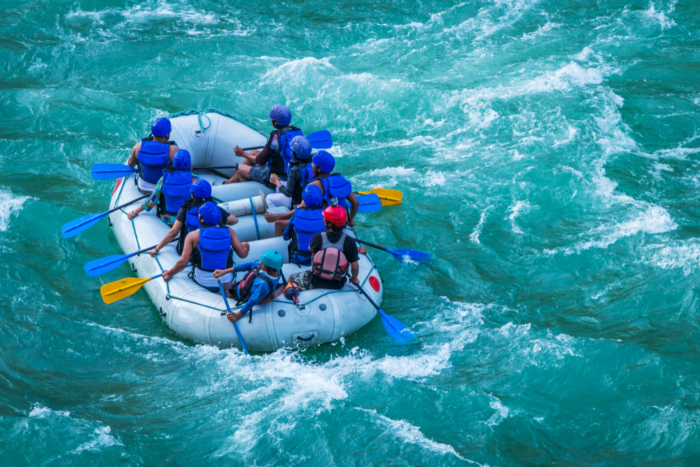 Aerial view of people in blue clothes and helmets white water rafting in rapids.