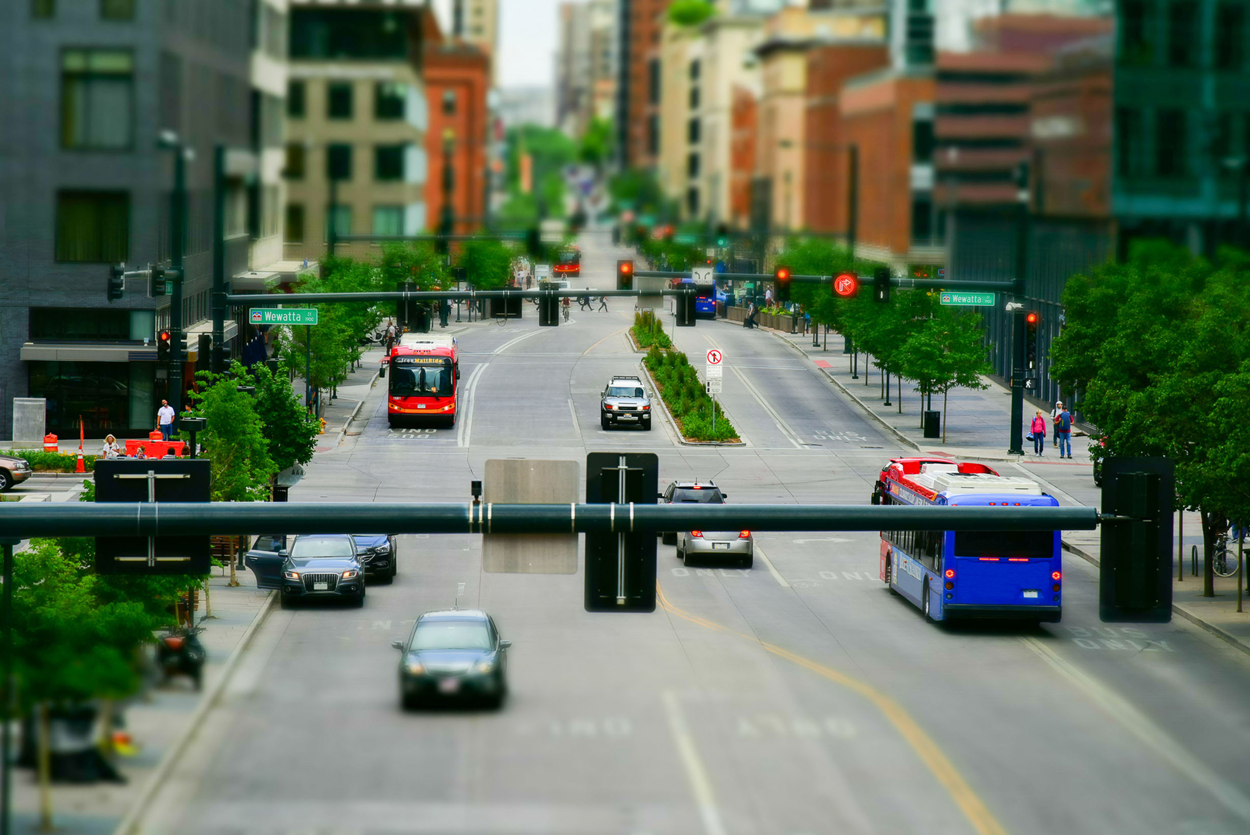 Cars, buses and people in an urban setting with busy streets and sidewalks.