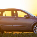 Gray car parked in countryside on blurred rural landscape and orange sky at sunset.