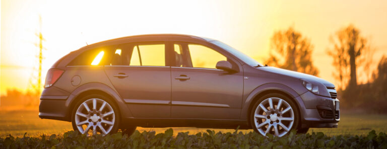 Gray car parked in countryside on blurred rural landscape and orange sky at sunset.