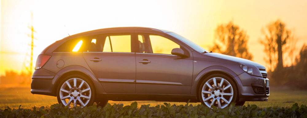 Gray car parked in countryside on blurred rural landscape and orange sky at sunset copy space background.
