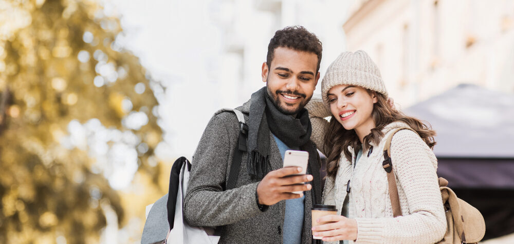Young joyful smiling woman and man looking at mobile phone in a city in autumn.