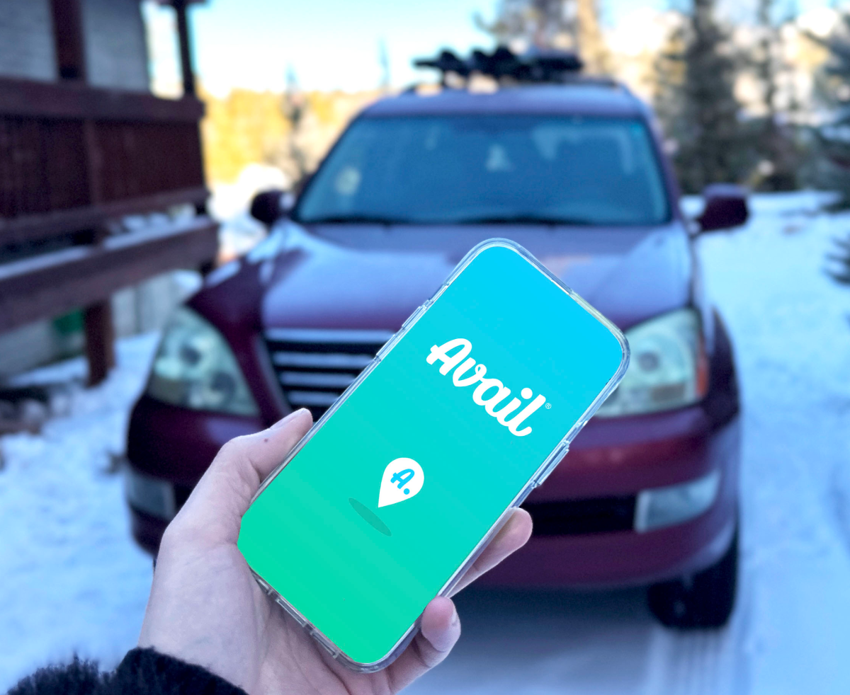 A hand holds a phone with the Avail car sharing logo in front of a red SUV.