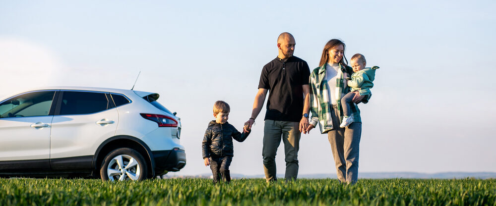 Family walks on the grass with a car parked in the background.